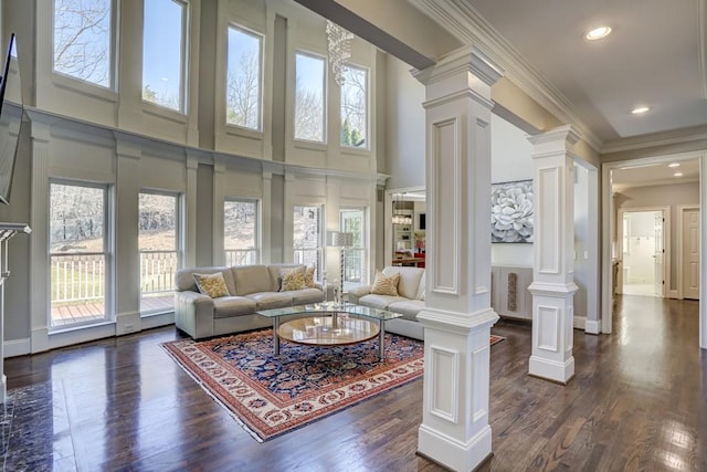 living room featuring a wealth of natural light, crown molding, ornate columns, and dark wood-style flooring