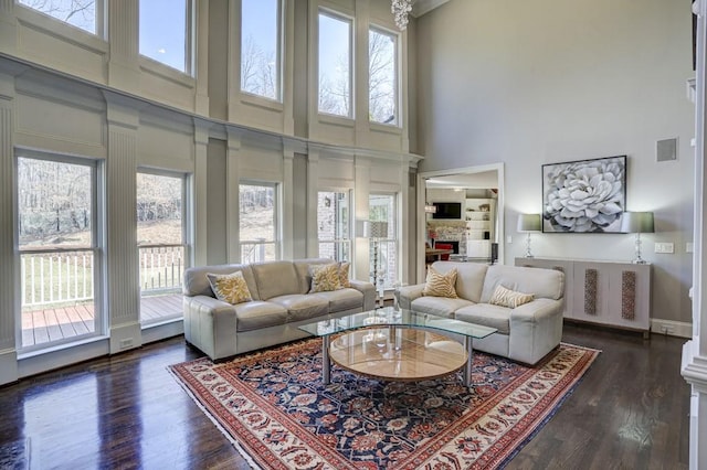 living area featuring a fireplace, a high ceiling, a healthy amount of sunlight, and dark wood-style flooring