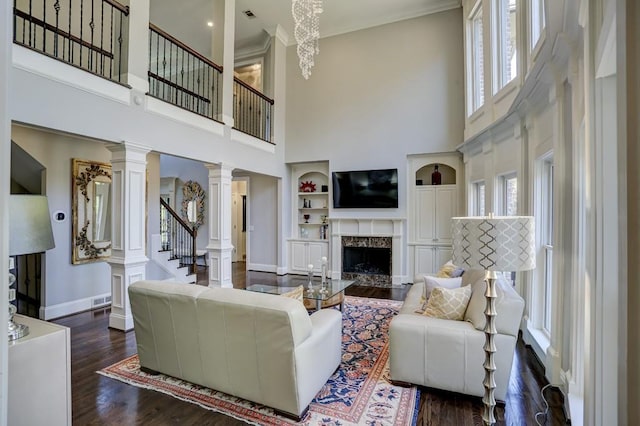 living area with crown molding, baseboards, dark wood finished floors, a premium fireplace, and decorative columns