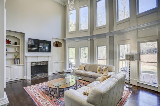 living room with a high end fireplace, dark wood finished floors, built in shelves, and a high ceiling