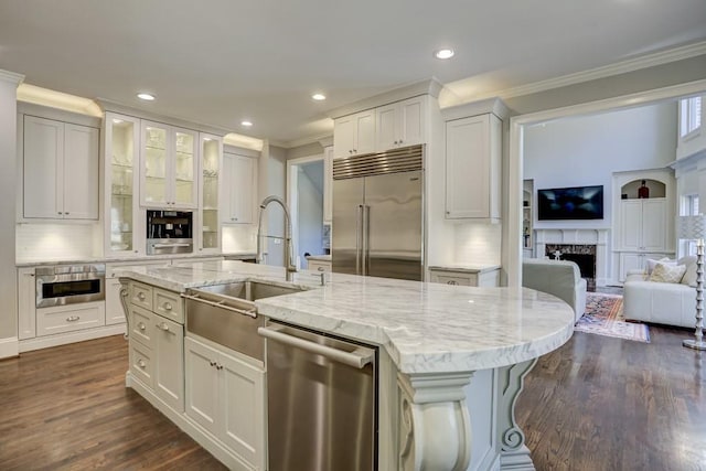 kitchen with a kitchen island with sink, a sink, white cabinetry, appliances with stainless steel finishes, and a fireplace