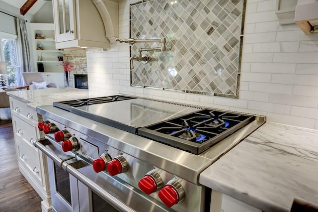 kitchen featuring double oven range, light stone countertops, white cabinets, glass insert cabinets, and tasteful backsplash