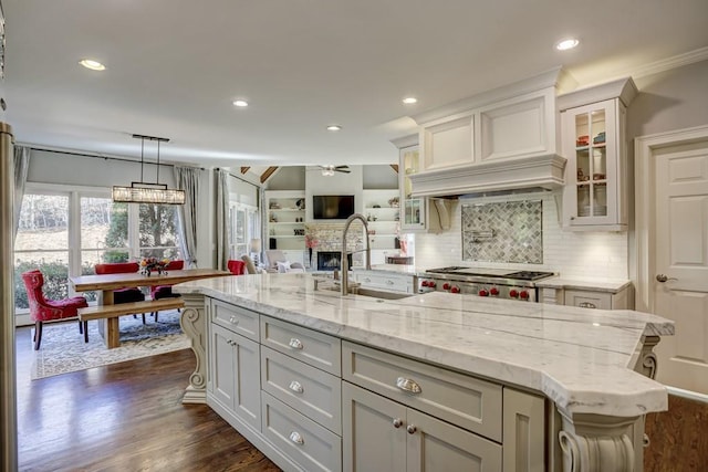 kitchen with light stone counters, a ceiling fan, dark wood-style flooring, a sink, and glass insert cabinets