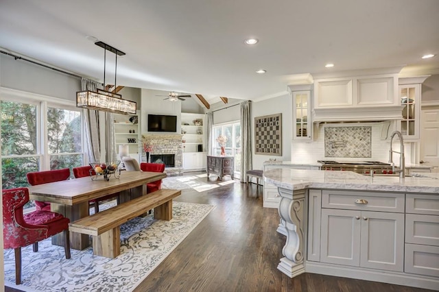 kitchen with a fireplace with raised hearth, ceiling fan, light stone counters, dark wood-style flooring, and a sink