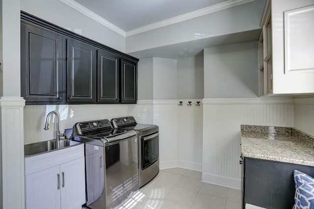 washroom with a wainscoted wall, cabinet space, ornamental molding, a sink, and washer and dryer