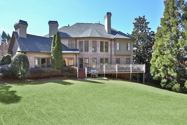 back of house featuring a yard, a shingled roof, a wooden deck, brick siding, and a chimney