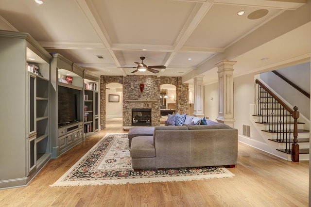 living area with wood finished floors, coffered ceiling, decorative columns, ceiling fan, and a stone fireplace