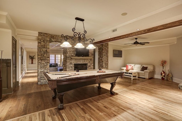 rec room with visible vents, a stone fireplace, wood finished floors, and crown molding