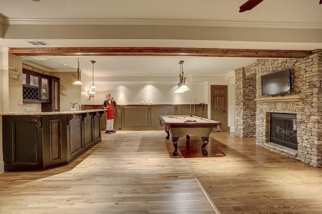 rec room with visible vents, ornamental molding, a stone fireplace, indoor wet bar, and light wood-type flooring