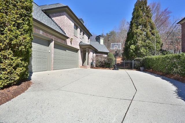 view of side of home featuring brick siding, an attached garage, concrete driveway, and fence