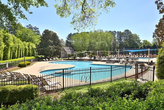 community pool featuring a patio, fence, and an outbuilding