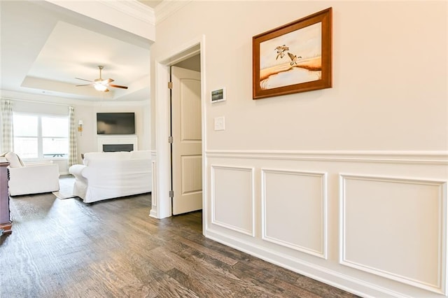 hall with dark wood-style floors, ornamental molding, a raised ceiling, wainscoting, and a decorative wall