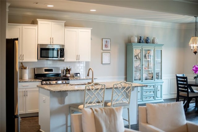 kitchen with stainless steel appliances, a sink, light stone countertops, ornamental molding, and white cabinets