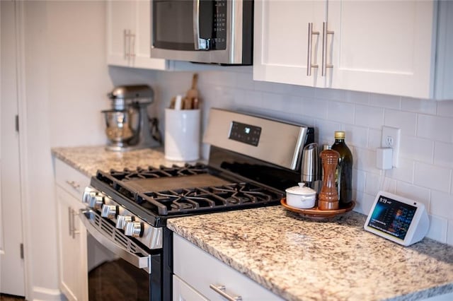 kitchen featuring appliances with stainless steel finishes, tasteful backsplash, white cabinetry, and light stone counters
