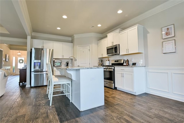 kitchen with appliances with stainless steel finishes, dark wood-style flooring, light stone countertops, ornamental molding, and a breakfast bar area