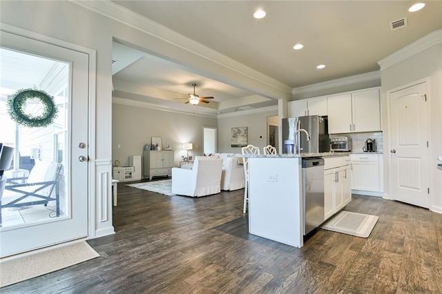 kitchen with appliances with stainless steel finishes, ornamental molding, open floor plan, an island with sink, and white cabinets