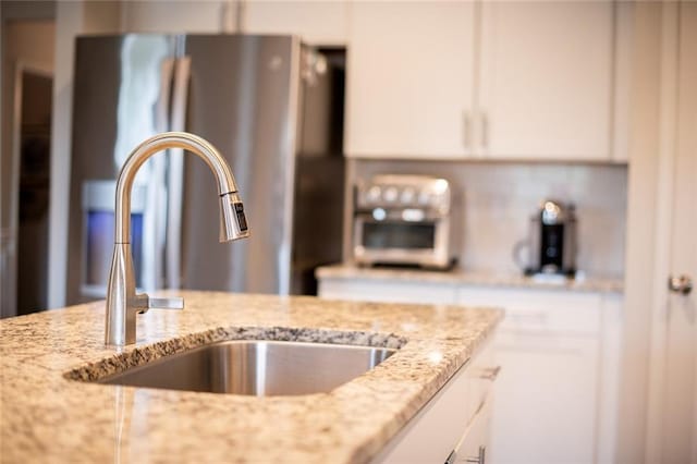 kitchen view of a sink, freestanding refrigerator, white cabinets, and light stone countertops