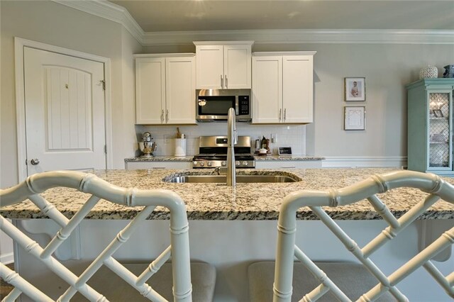 kitchen with appliances with stainless steel finishes, decorative backsplash, a sink, light stone counters, and white cabinets