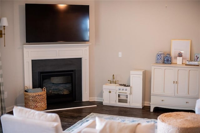 living area featuring dark wood-type flooring, a glass covered fireplace, and baseboards