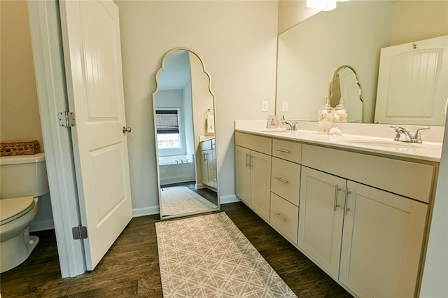 bathroom with toilet, wood finished floors, double vanity, and baseboards