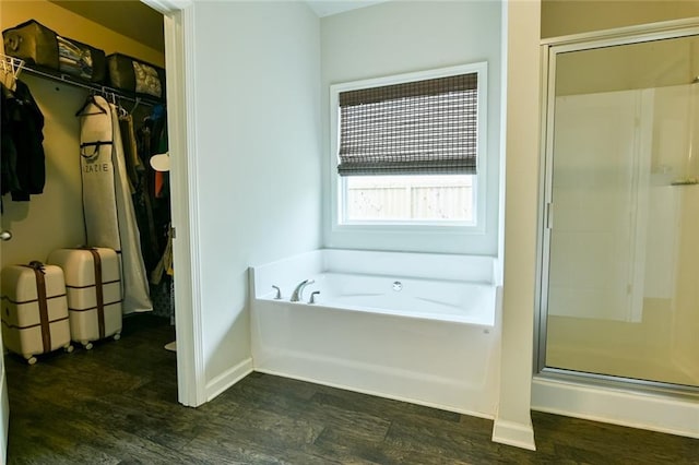 full bathroom featuring a shower stall, a spacious closet, wood finished floors, a bath, and baseboards