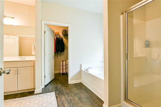 full bathroom with wood finished floors, a shower stall, a garden tub, vanity, and a spacious closet