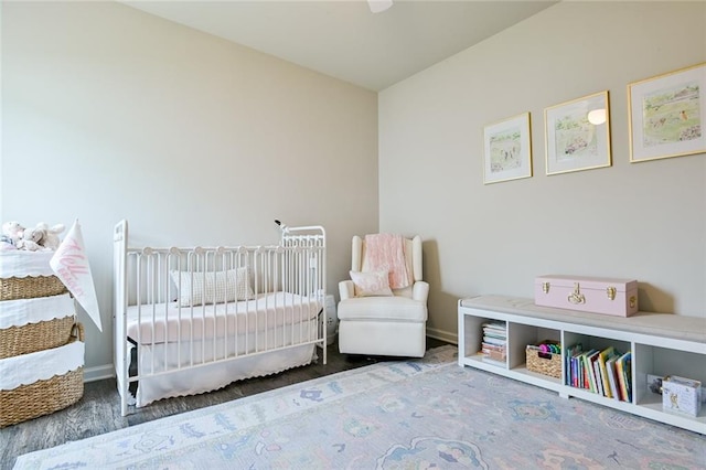 bedroom featuring baseboards, wood finished floors, and a nursery area