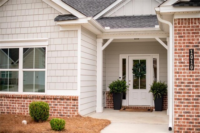 property entrance with roof with shingles, brick siding, and board and batten siding