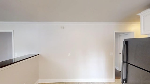 interior space with baseboards, ornamental molding, freestanding refrigerator, and white cabinets