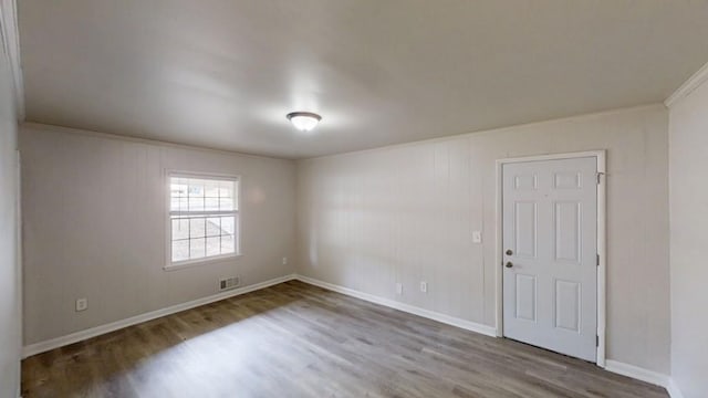 empty room featuring ornamental molding, visible vents, baseboards, and wood finished floors