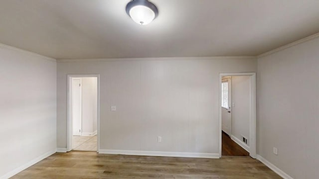 empty room featuring baseboards, visible vents, wood finished floors, and ornamental molding