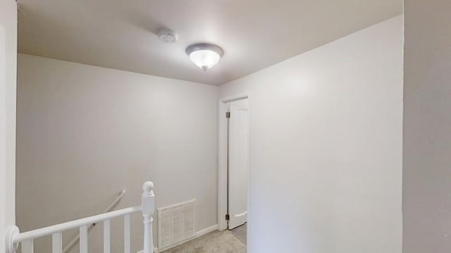 hallway featuring light colored carpet, visible vents, and baseboards