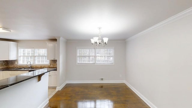 unfurnished dining area featuring light wood-style flooring, crown molding, baseboards, and a sink