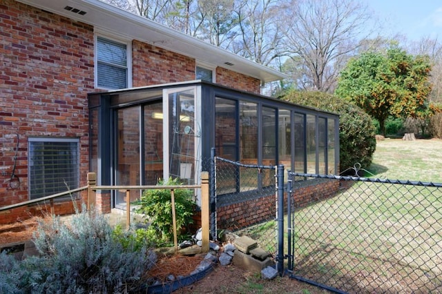 view of side of home featuring a sunroom, a gate, fence, and brick siding