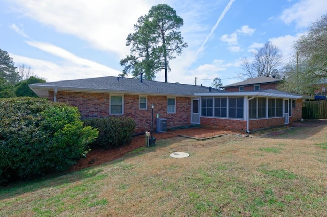 rear view of property with a sunroom, brick siding, central AC, and a yard