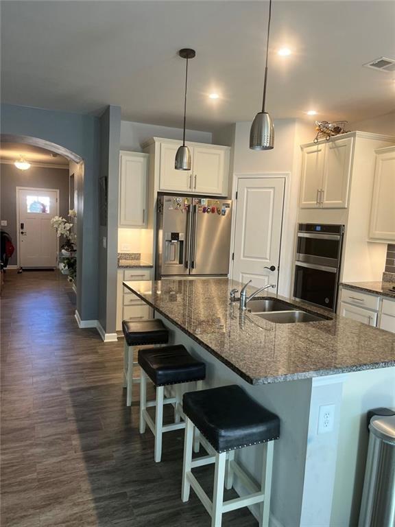 kitchen with a sink, dark wood finished floors, visible vents, arched walkways, and appliances with stainless steel finishes
