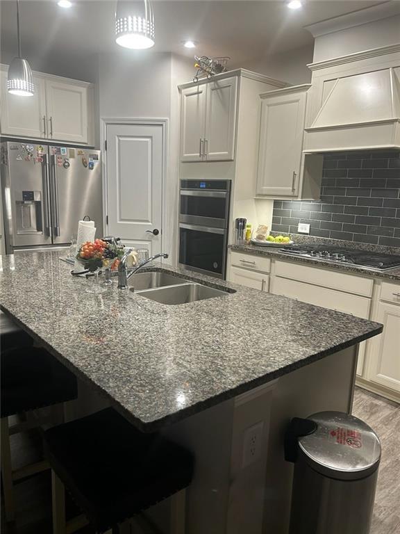 kitchen with dark stone counters, appliances with stainless steel finishes, a sink, and a kitchen bar