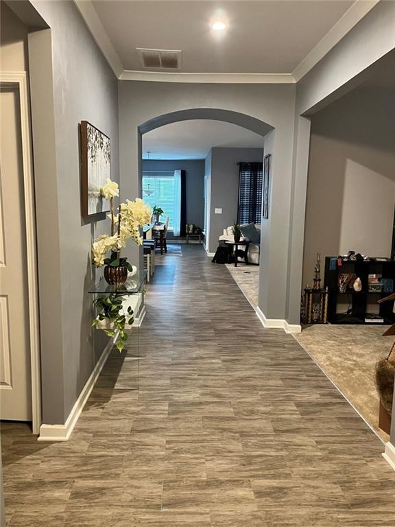 hall featuring arched walkways, ornamental molding, visible vents, and wood finished floors