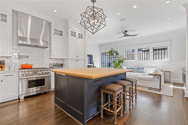 kitchen featuring crown molding, high end stainless steel range, butcher block countertops, white cabinets, and wall chimney exhaust hood