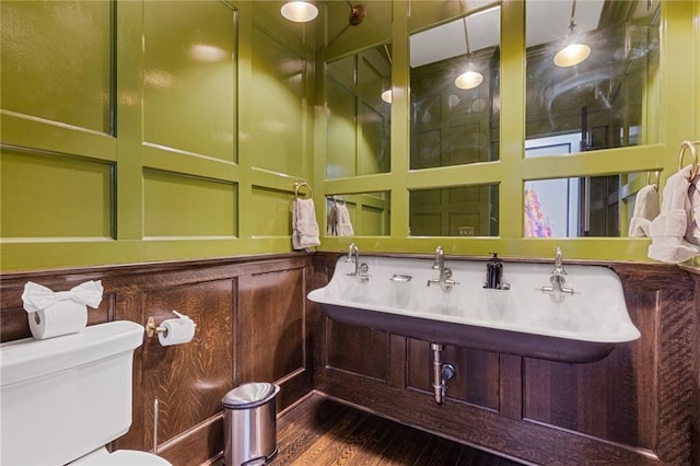 half bath featuring toilet, wood finished floors, and a decorative wall