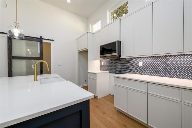 kitchen featuring sink, hanging light fixtures, tasteful backsplash, a barn door, and white cabinets