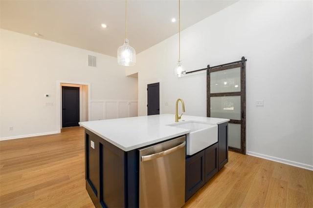 kitchen with a kitchen island with sink, sink, a barn door, dishwasher, and hanging light fixtures