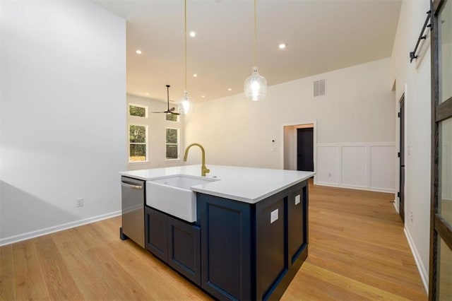 kitchen with stainless steel dishwasher, a kitchen island with sink, sink, a barn door, and decorative light fixtures