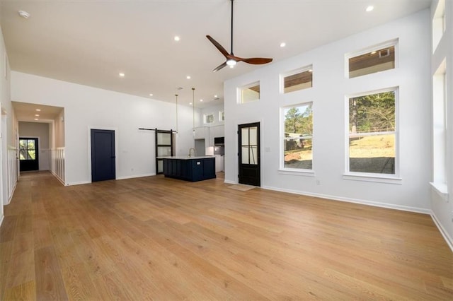 unfurnished living room with ceiling fan, light hardwood / wood-style flooring, a high ceiling, and sink