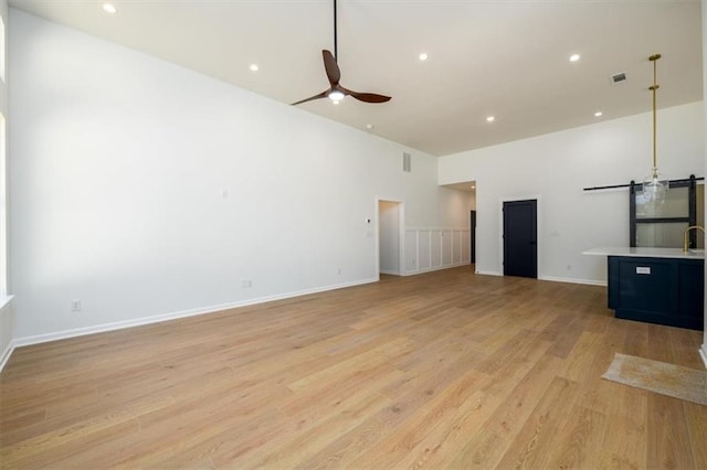 unfurnished living room featuring ceiling fan, a high ceiling, and light wood-type flooring