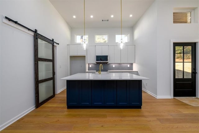 kitchen with decorative light fixtures, a barn door, white cabinetry, and light hardwood / wood-style flooring