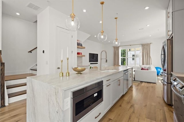 kitchen featuring white cabinets, sink, a kitchen island with sink, pendant lighting, and light wood-type flooring