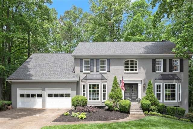 colonial inspired home with french doors, a garage, brick siding, concrete driveway, and a shingled roof