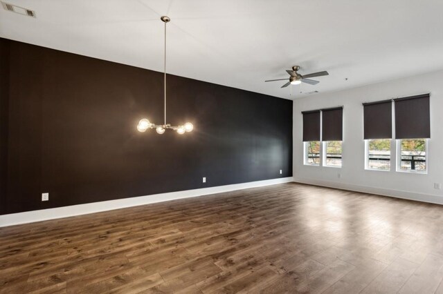 empty room with ceiling fan with notable chandelier and dark hardwood / wood-style floors