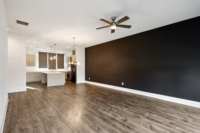 unfurnished living room featuring ceiling fan with notable chandelier and dark hardwood / wood-style flooring